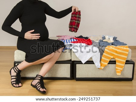 Pregnant woman looking at newborn clothes for her future baby, mother searching her new wardrobe for her infant