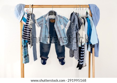 Dressing closet with clothes arranged on hangers.Blue and white wardrobe of newborn,kids, toddlers, babies full of all clothes.Many t-shirts,pants, shirts,blouses,blue hat, onesie hanging