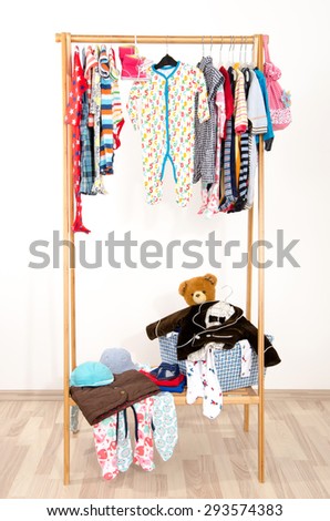Dressing closet with clothes arranged on hangers.Colorful wardrobe of newborn,kids, toddlers, babies on a rack.Many t-shirts,pants, shirts,blouses, onesie hanging. Messy clothes thrown on a shelf