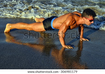 Strong bodybuilder with six pack.Fitness trainer with perfect abs, shoulders,biceps, triceps,chest, flexing his muscles on the beach, training in vacation, doing push ups in the sand