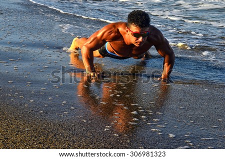 Strong bodybuilder with six pack.Fitness trainer with perfect abs, shoulders,biceps, triceps,chest, flexing his muscles on the beach, training in vacation, doing push ups in the sand