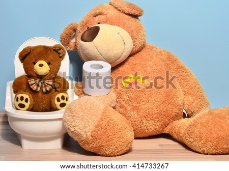 Small teddy bear sitting on the potty and playing with toilet paper, father bear teaching his cute kid how to pee and poo
