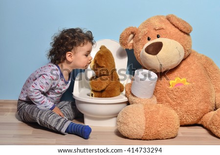 Baby toddler sitting on the floor near a potty and kissing a teddy bear. Cute kid potty training for pee and poo helped by teddy bear who gives him toilet paper