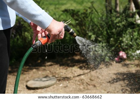 Living with pain series. Senior woman with rheumatoid arthritis watering the garden.