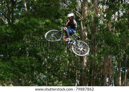 Teenage male doing high jump on a bmx bike in a forestry area