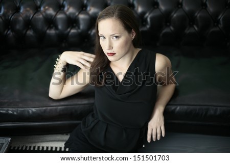 Portrait of a beautiful girl  in black looking up , leaning on black leather couch