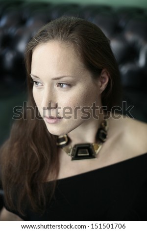 Portrait of a beautiful girl  in black looking away, leaning on black leather couch in background