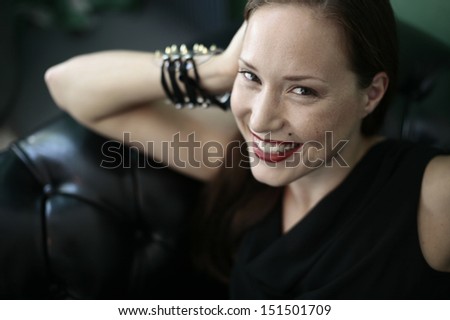 Portrait of a beautiful girl smiling dressed in black  looking up , leaning on black leather couch