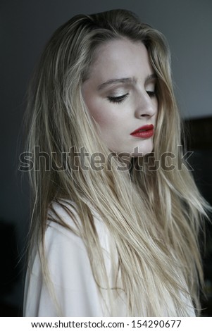 photo of beautiful young woman with long blond hair in a white shirt, looking down, fashion portrait