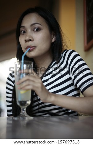 Asian girl drinking lemonade in the garden restaurant, surprised and shocked, beautiful girl in a sailor\'s T-shirt
