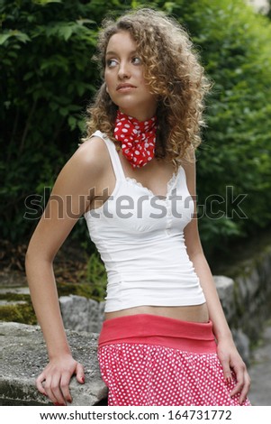 girl in white shirt and red scarf around the neck sitting on the fence looking away