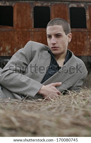 Young Man Lying On The Grass,  young man in a checkered jacket lying on the grass, behind an old wagon from the train , Autumn winter man portrait lying in golden grass
