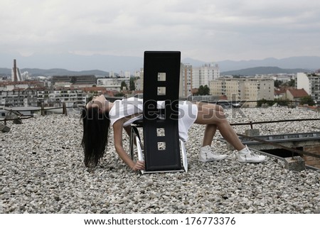image of young woman in white lying over chair looking up , leaning on black leather chair on the top of the building