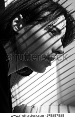 image of a young woman with shadow stripes  by the window looking away black and white