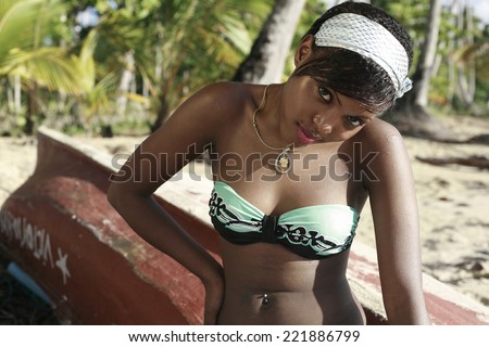 beautiful fashion girl  dressed in bikini sitting on the old red boat at the beach , fashion photo of sensual beautiful woman with dark hair posing in water on summer beach in sunlight rays