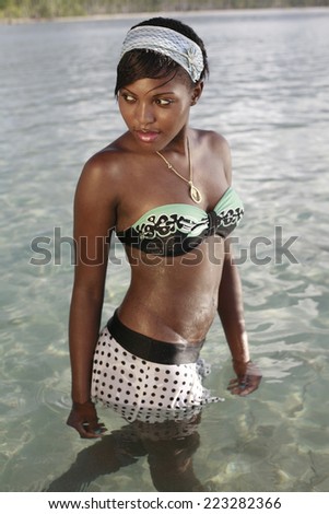 latin girl dressed in bikini at the beach posing in the water , fashion photo of sensual beautiful latin woman with dark hair posing in water on summer beach in sunlight rays