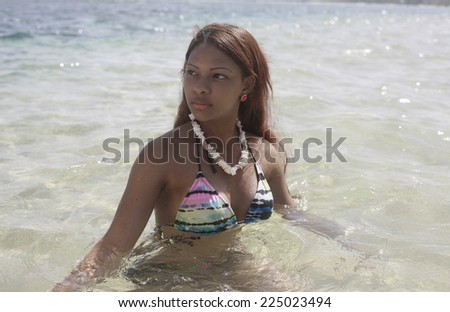 young latin woman dressed in bikini at the beach posing in the water , fashion photo of sensual beautiful latin woman with dark hair posing in water on summer beach in sunlight rays