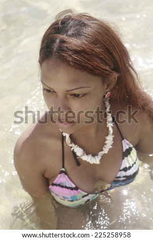 latin woman with white necklace dressed in bikini at the beach posing in the water , fashion photo of sensual beautiful latin woman with dark hair posing in water on summer beach in sunlight rays