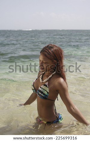 Latina in bikini coming out from water, girl in swimsuit wearing necklace walking out of water on sandy beach