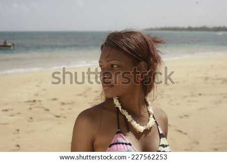 Latina in bikini playing in water, girl in swimsuit wearing necklace walking out of water on sandy beach