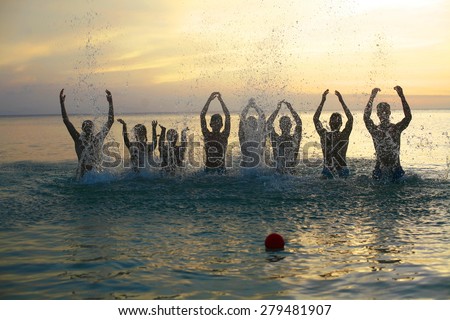 group of young people fun on the beach , making fun and playing in water, jumping out of water on sandy beach,  fashion photo of group of young people playing in water on summer beach in sunlight rays