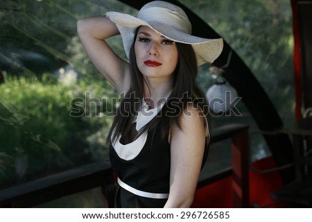 young lady with white hat on the river boat looks down  young beautiful woman on a river boat posing dressed in brightly colored clothing,