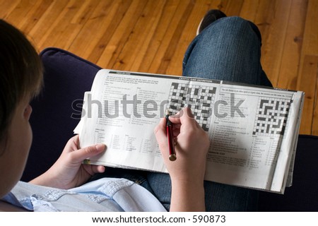 A lady sitting on a sofa doing the crossword casually on her knee.