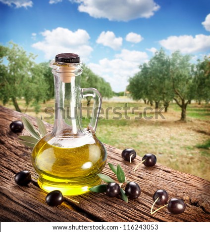Black olives with bottle of oil on a wooden table on a background of olive garden.