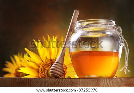 Honey in a glass jar and flower sunflower on a wooden table.
