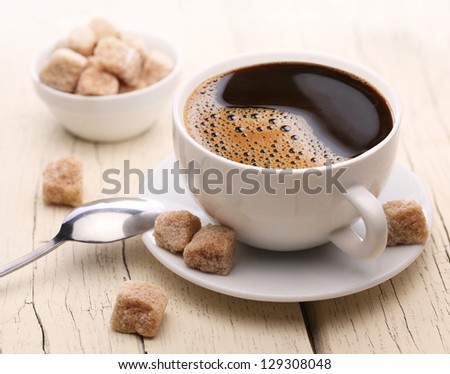 Cup of coffee with brown sugar on a light wooden table.