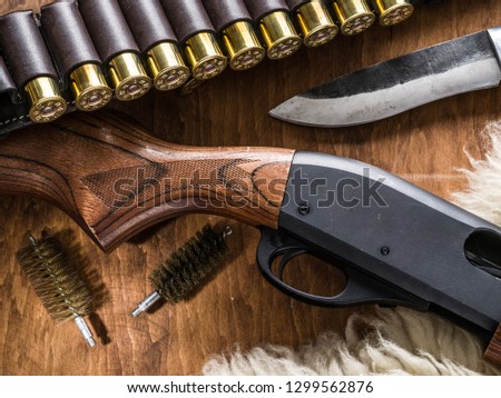 Hunting equipment - pump action shotgun, cartridge 12 guage and hunting knife on the wooden table.