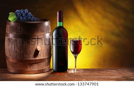 Bottle and a glass of wine with a wooden barrel on dark yellow background with a gradient.