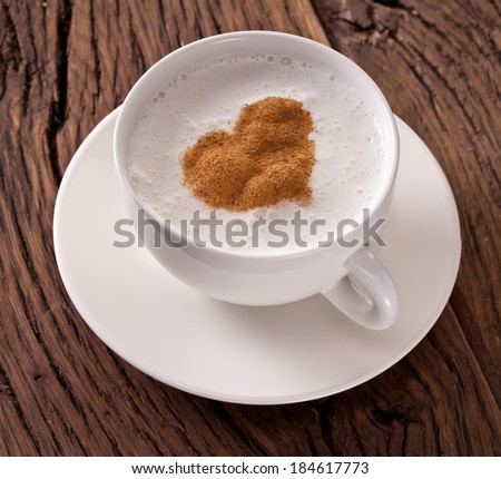 Cup of cappuccino with ground cinnamon in the form of heart on old wooden table. Top view.