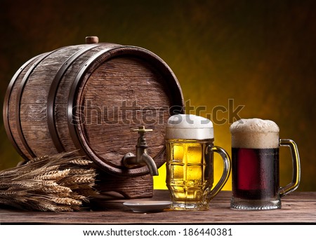 Beer glasses, old oak barrel and wheat ears on wooden table.