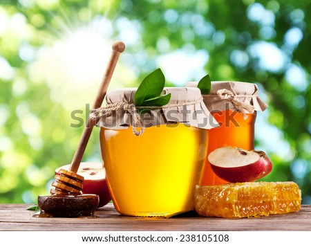 Glass cans full of honey, apple and combs on wooden table at the garden.