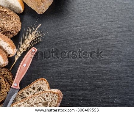 Bread slices, a wheat and a knife on the black stone desk.
