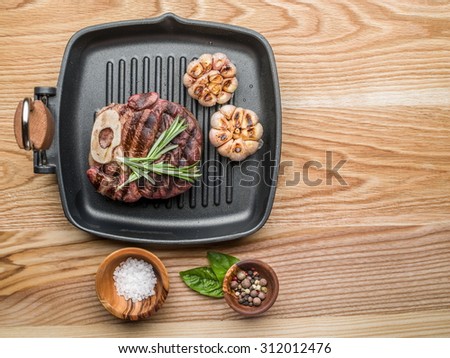 Beef steak with spices on pan on wooden table.