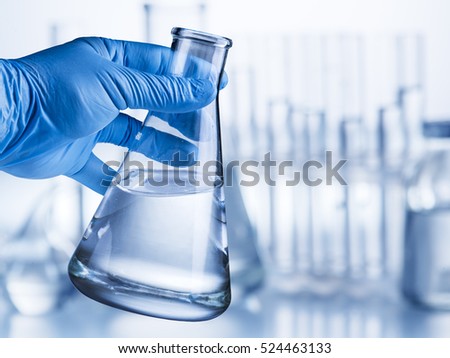 Laboratory beaker in analyst\'s hand in plastic glove.