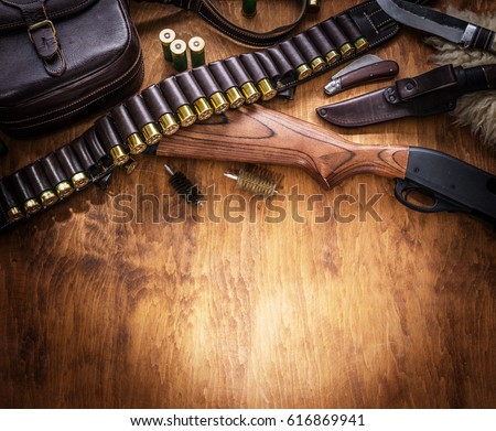 Hunting equipment - pump action shotgun, 12 mm hunting cartridge  and hunting knife on the wooden table.