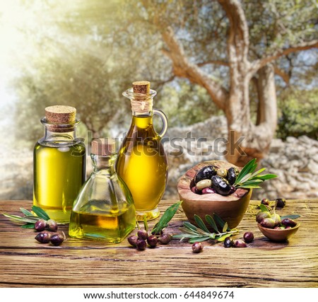 Olive berries in the wooden bowl and bottles of olive oil on the table. The beautiful sunset in the background.