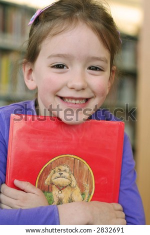 smiling little girl hugging a book at the library