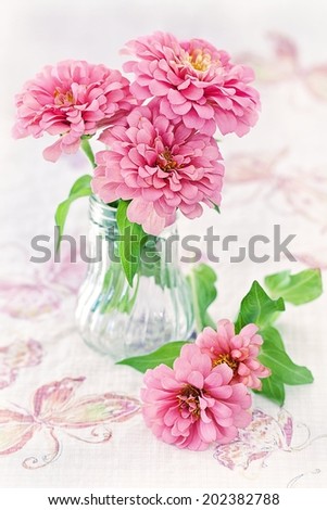 beautiful pink flowers in a glass vase on a beautiful tablecloth