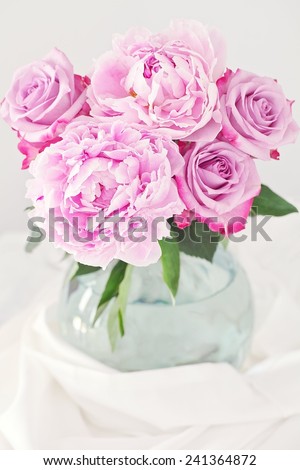 Floral composition with a pink peony and roses in a glass vase.