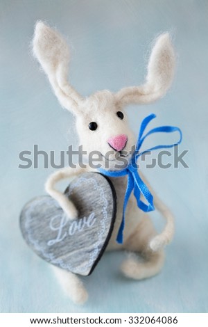 Felted wool toy.Woolen handmade toy bunny with a wooden heart on a blue background .