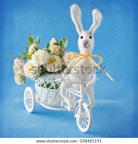 Felted wool toy.Woolen handmade toy bunny on a bicycle with flowers , blue background with a texture .