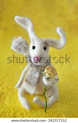 Homemade toy rabbit with a bouquet of flowers on a yellow background .Felted wool toy.