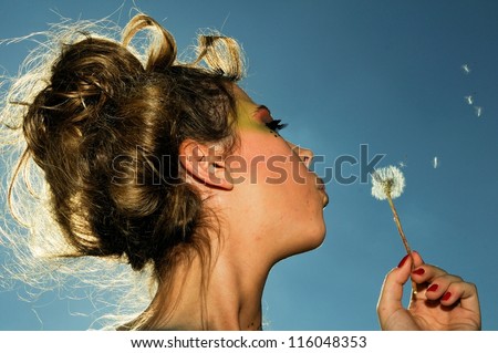 Close-up of an attractive women blowing a dandelion