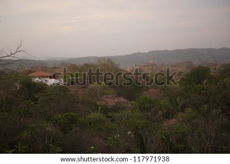 Sun fading over a white house with an orange roof in the rolling hills above the treetops of Costa Rica