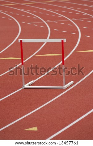 A red and white hurdle in a lane, on a synthetic track