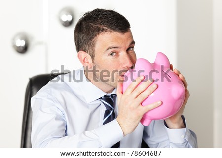 young man in office kissing a pink piggy bank